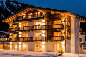A multi-story hotel with balconies, large windows, and a snow-covered ground. - NATURPARKGUT - alpdeluxe Apartments (Holzgau)