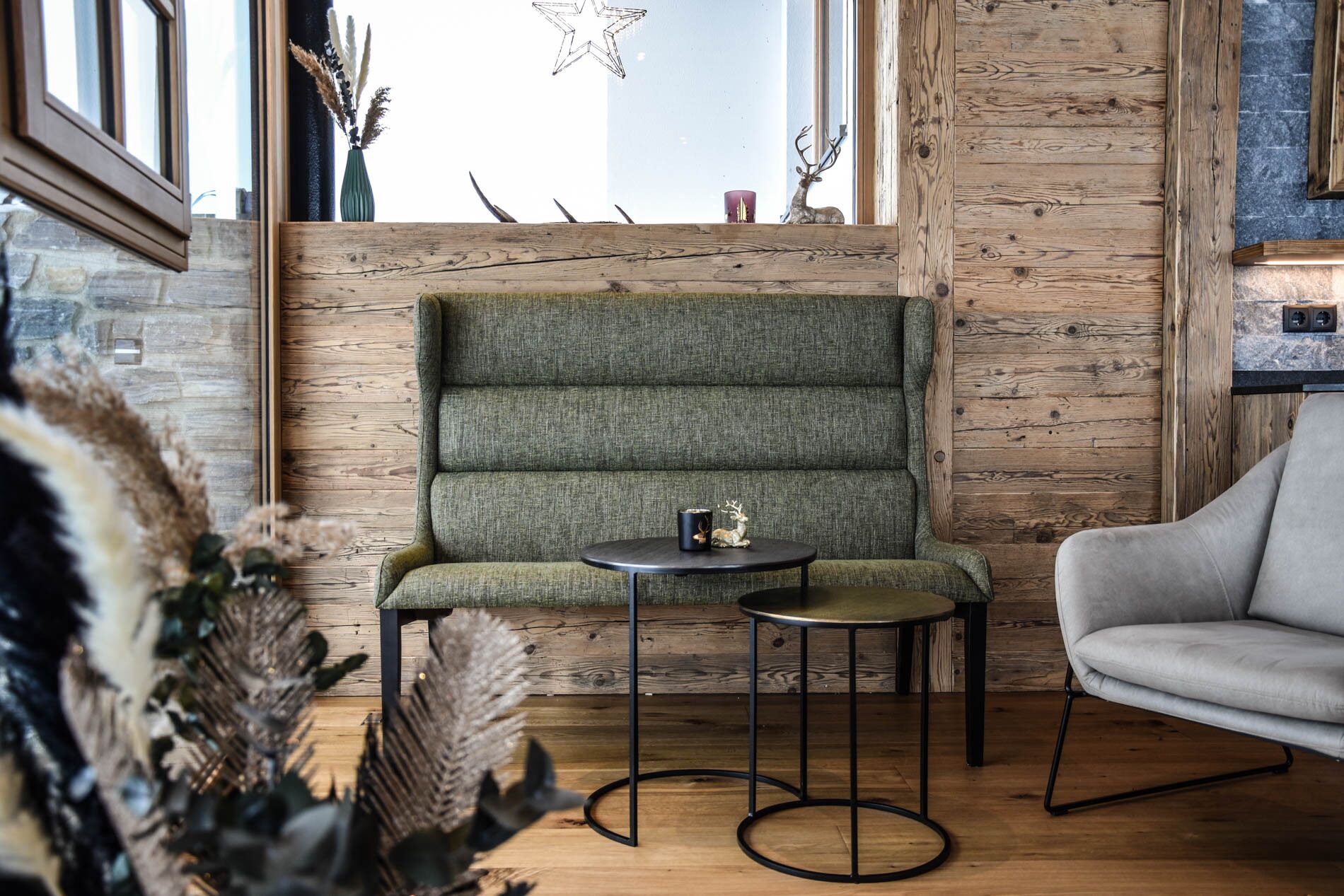 Un rincón acogedor con un banco tapizado en verde, una mesa redonda y un sillón gris.