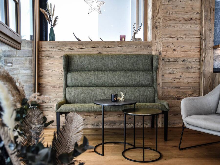 A cozy seating area with a green upholstered bench, a round table, and a grey armchair.