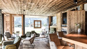 A spacious room with wooden ceiling and walls, large windows offering a view of the outdoors, and a bar area with seating.