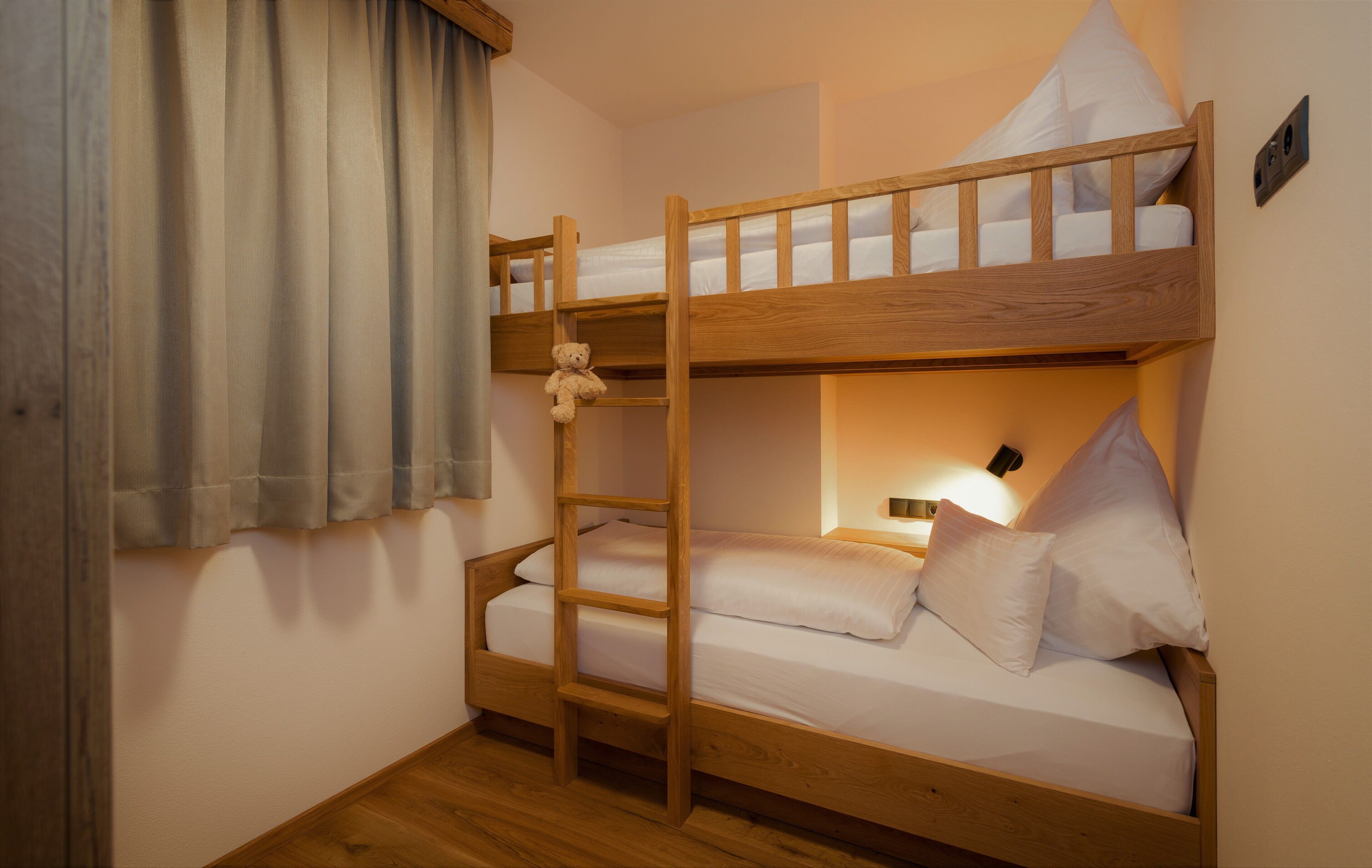 A bunk bed room with a ladder, a window with curtains, and a wall-mounted light.