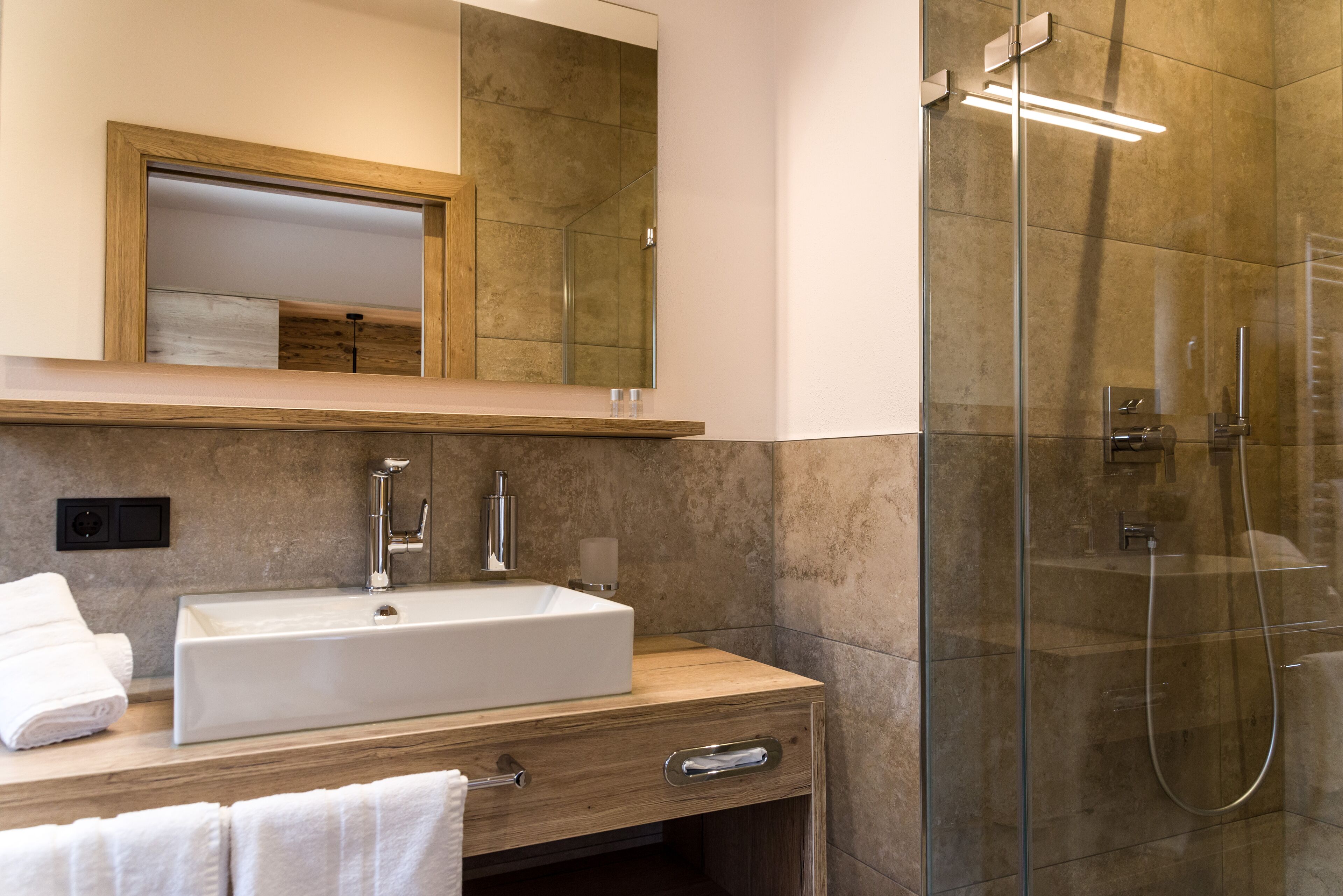 Un baño moderno con un lavamanos rectangular, un espejo y una ducha con mampara de vidrio.