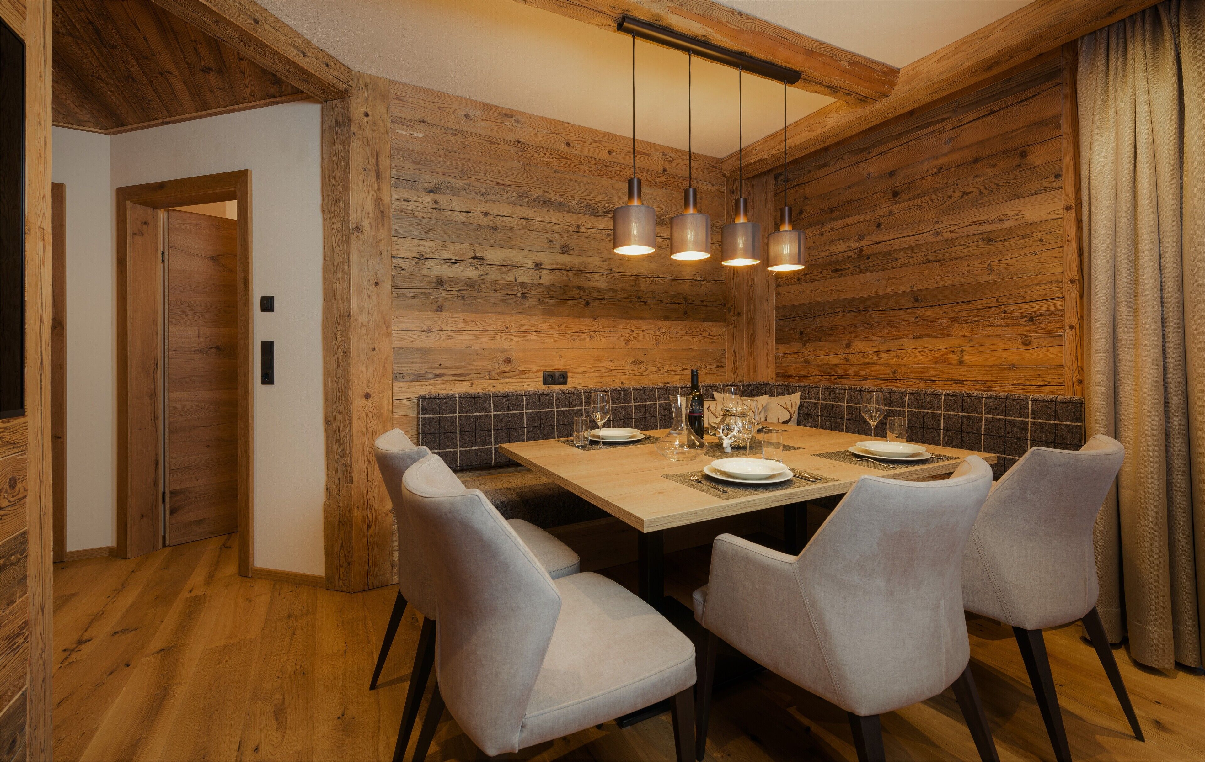 A wooden-paneled dining room with a wooden table set for four, grey upholstered chairs, and pendant lighting.
