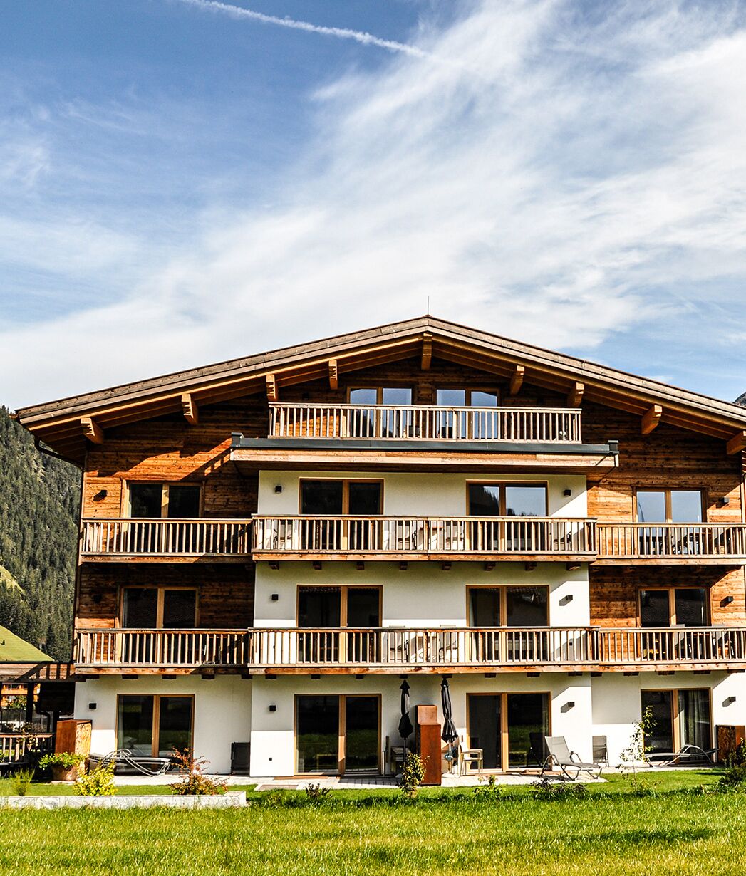 A multi-story wooden chalet with balconies, large windows, and a grassy front yard.