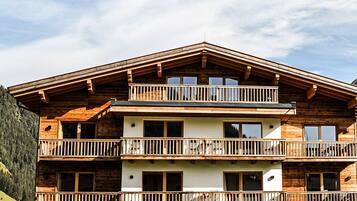 A multi-story wooden chalet with balconies, large windows, and a grassy front yard.