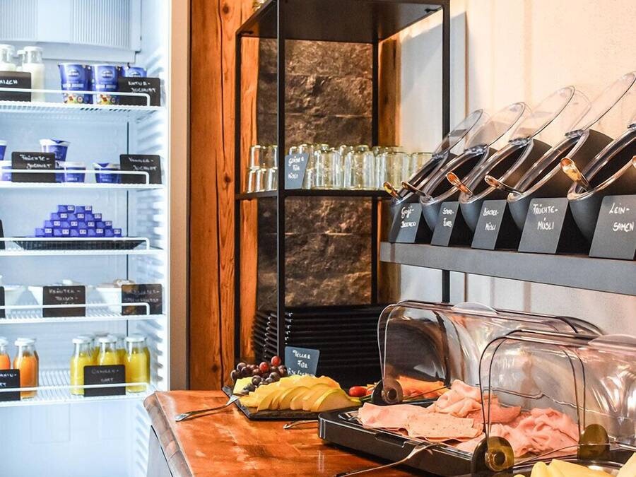 A buffet area with a variety of food options, including fruits, cheeses, and meats, and a refrigerator stocked with beverages.