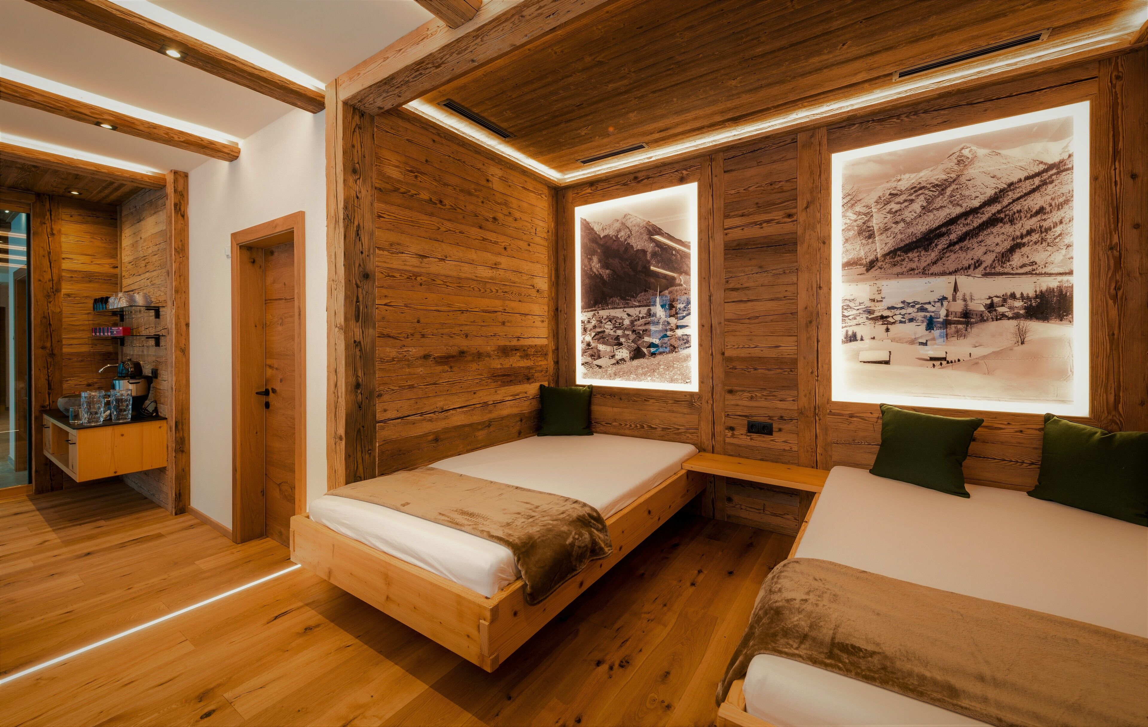 Una habitación tipo cabaña de madera con dos camas, un banco de madera y una pequeña mesa con bebidas.