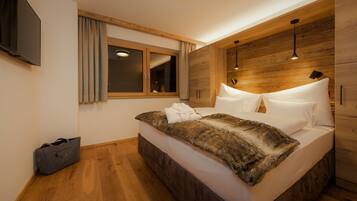 Une chambre à coucher moderne avec une tête de lit en bois, un grand lit avec du linge de lit blanc, une fenêtre avec des rideaux et un téléviseur à écran plat fixé au mur.