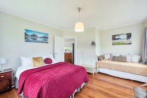 A bedroom with a bed, a sofa, a hanging light, and two paintings on the walls.