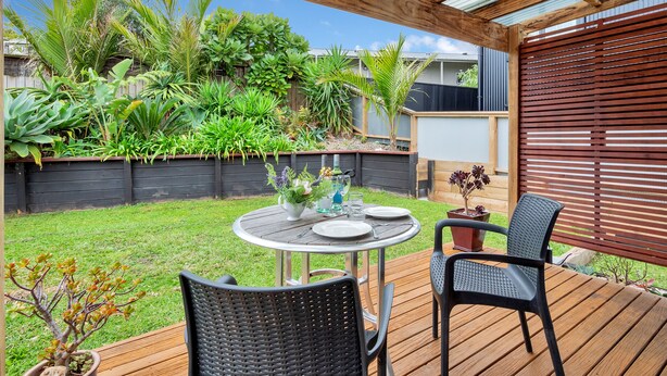 A covered patio with a round table, two chairs, and a variety of plants. - Sunny Grey Lynn Holiday Home (Auckland)