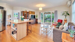 A modern kitchen with a central island, a dining area with a sofa and table, and a living room with a couch and a TV. - Sunny Grey Lynn Holiday Home (Auckland)