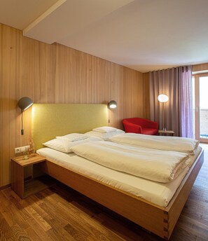 Habitación de hotel con cabecera de madera, cama con ropa blanca, una silla roja y dos lámparas de noche.