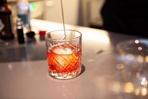 Un vaso transparente con un diseño geométrico, conteniendo un líquido rojo, siendo servido desde una botella.