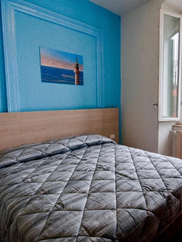 A bed with a quilted cover, a blue wall with a framed picture, and a window with a view of the sky.