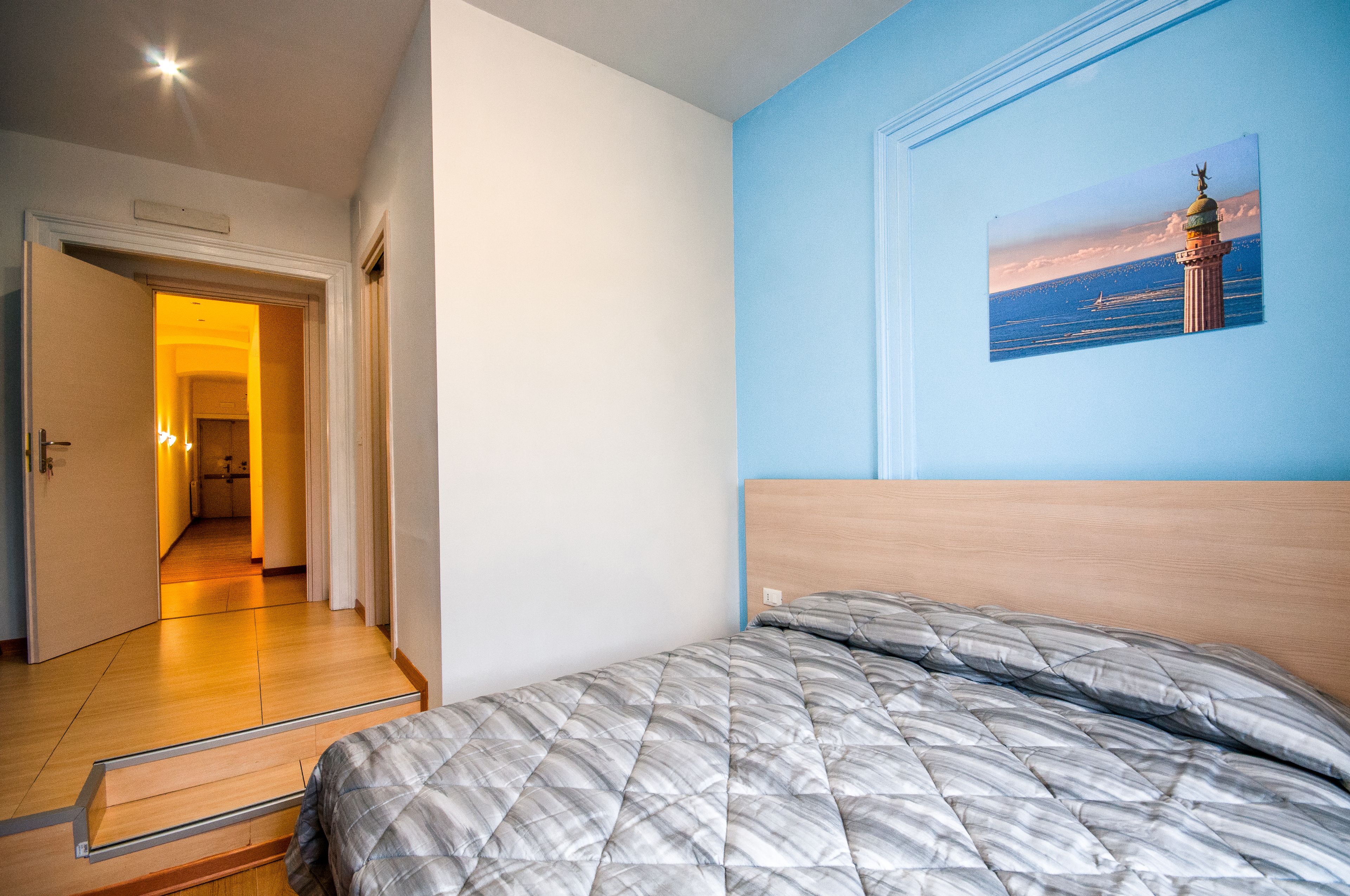 Een slaapkamer met een bed, een gang die naar een andere kamer leidt, en een muur met een afbeelding van een vuurtoren.