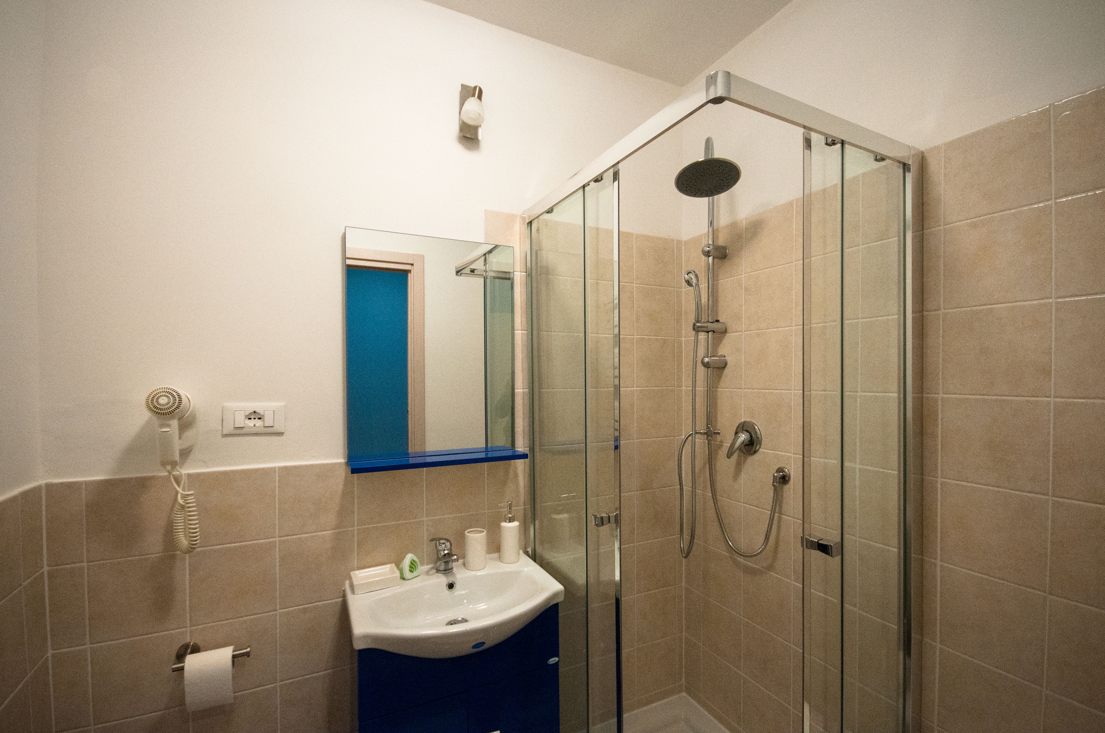 A bathroom with a glass-enclosed shower, a sink with a mirror, and a blue door.