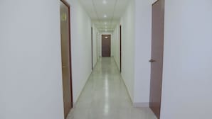 Un pasillo largo y estrecho con paredes blancas y suelo de baldosas, que conduce a una puerta al final.