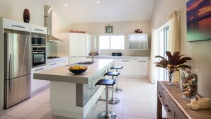 A modern kitchen with a central island, stainless steel appliances, and a 'KISS THE COOK' sign. - Kakaia Retreat (Rarotonga)