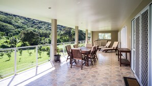 A covered patio with a stone floor, a table with chairs, and a view of a lush green landscape. - Kakaia Retreat (Rarotonga)