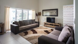 A living room with a sofa set, a flat-screen TV, a decorative wall piece, and a patterned rug. - Kakaia Retreat (Rarotonga)