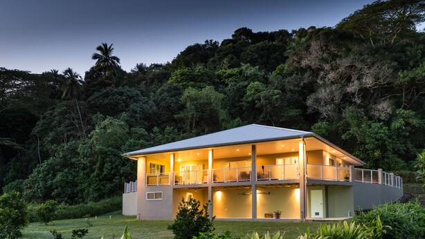 A two-story house with a balcony, surrounded by lush greenery and a hill in the background. - Kakaia Retreat (Rarotonga)