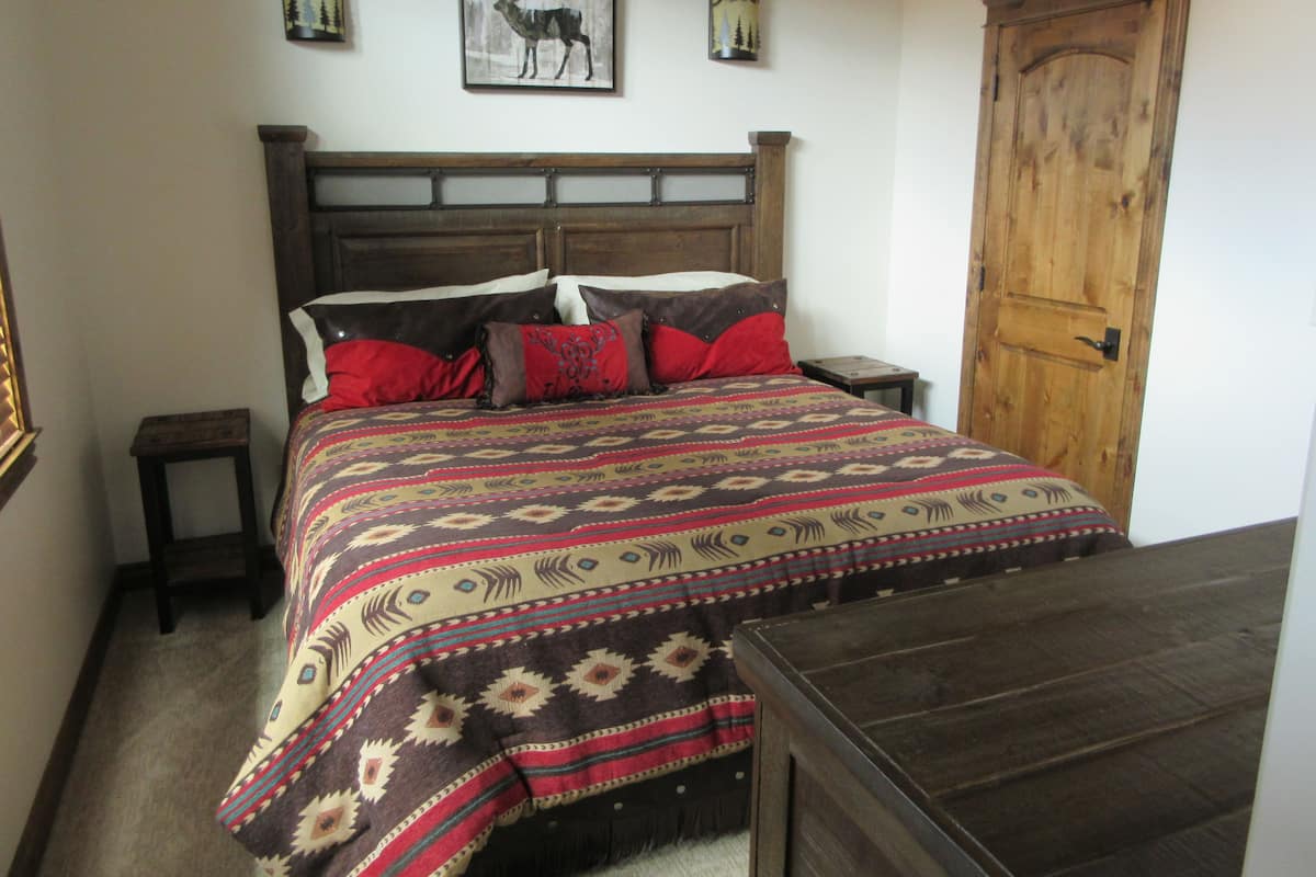 A bedroom with a large bed, wooden headboard, two bedside tables, a nightstand, a wooden door, and two wall-mounted lamps.