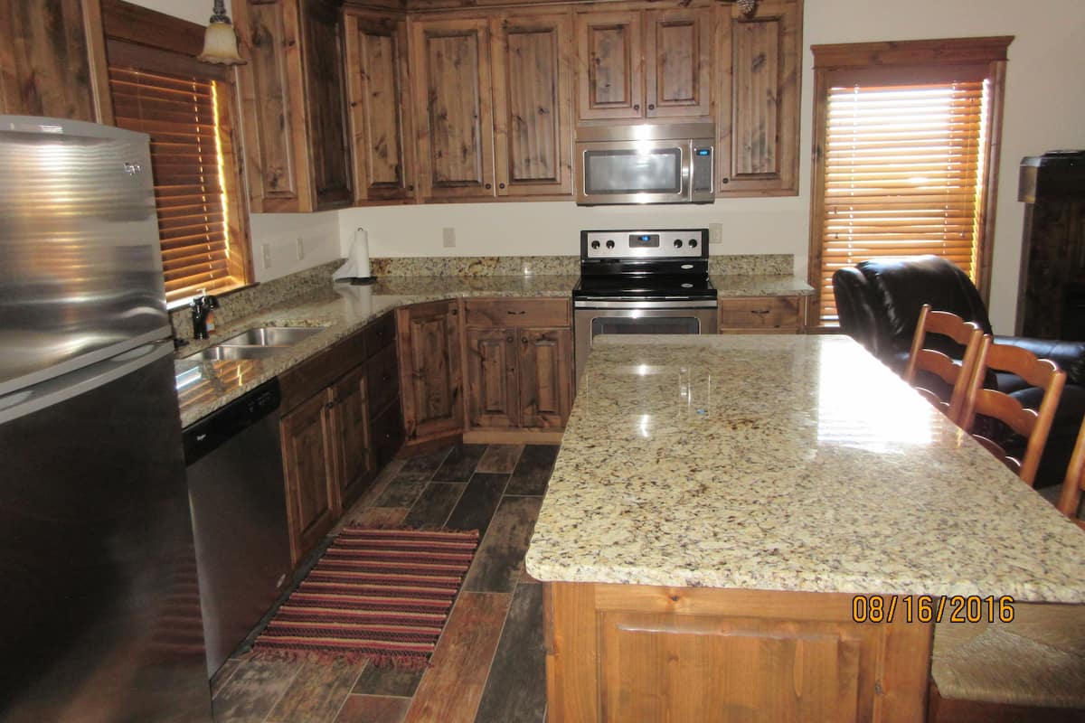 A kitchen with wooden cabinets, a granite countertop, stainless steel appliances, and a dining area with chairs.