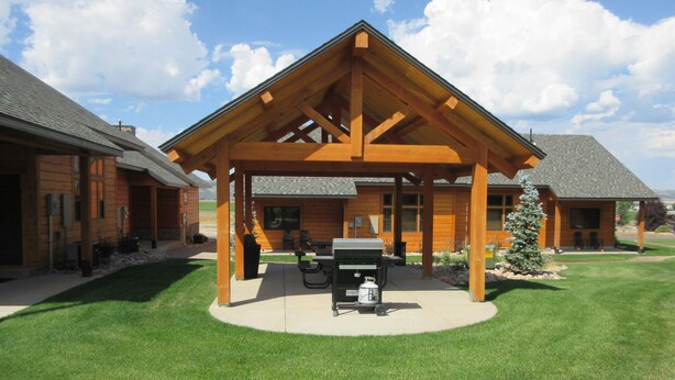 A wooden lodge with a covered patio, a barbecue grill, and a small Christmas tree. - Townhomes on the Green (Afton)