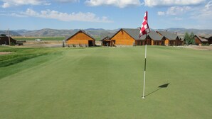 A golf course with wooden cabins in the background. - Townhomes on the Green (Afton)