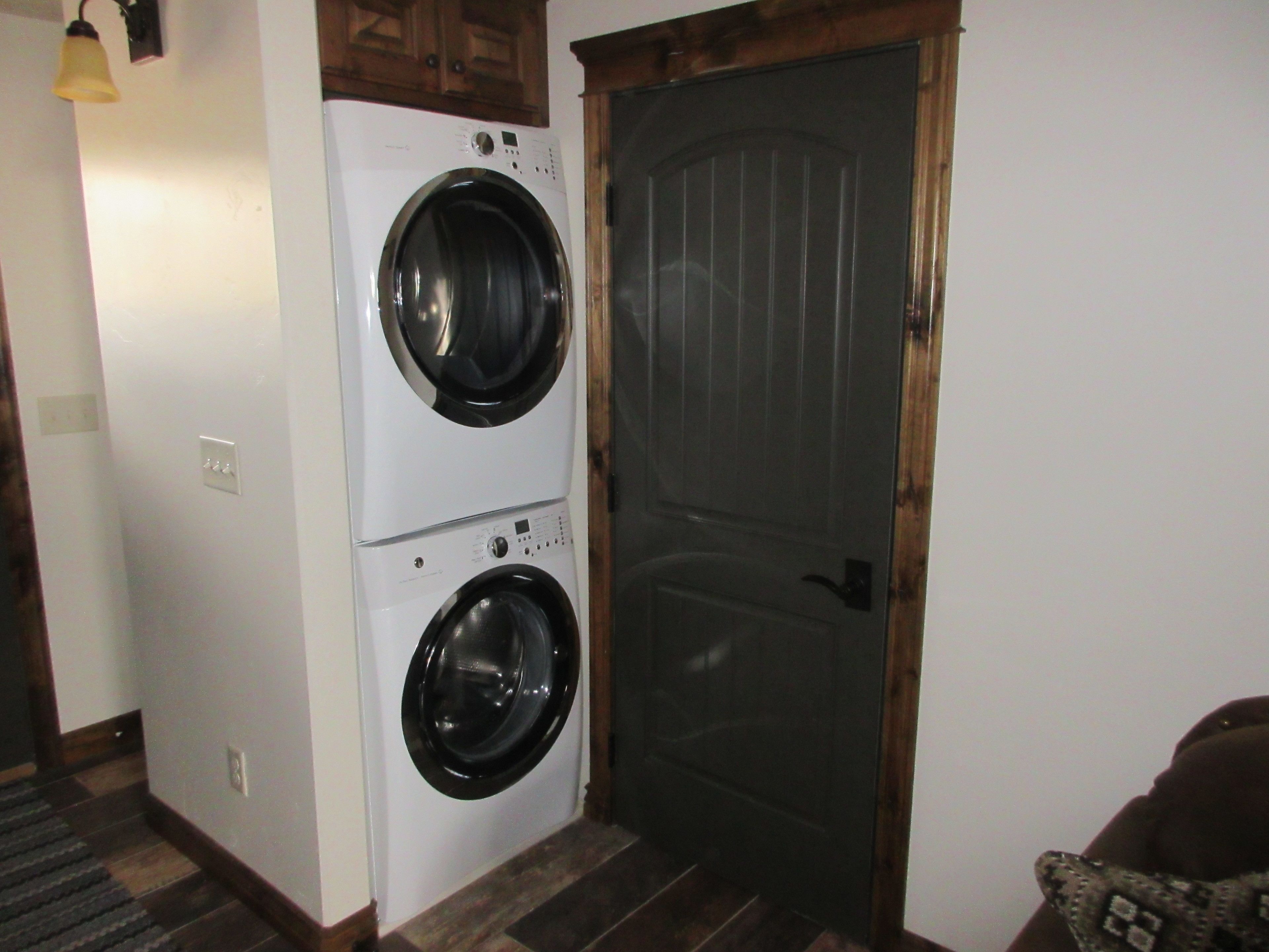 A laundry room with two stacked front-loading washing machines and a door with a wooden frame.