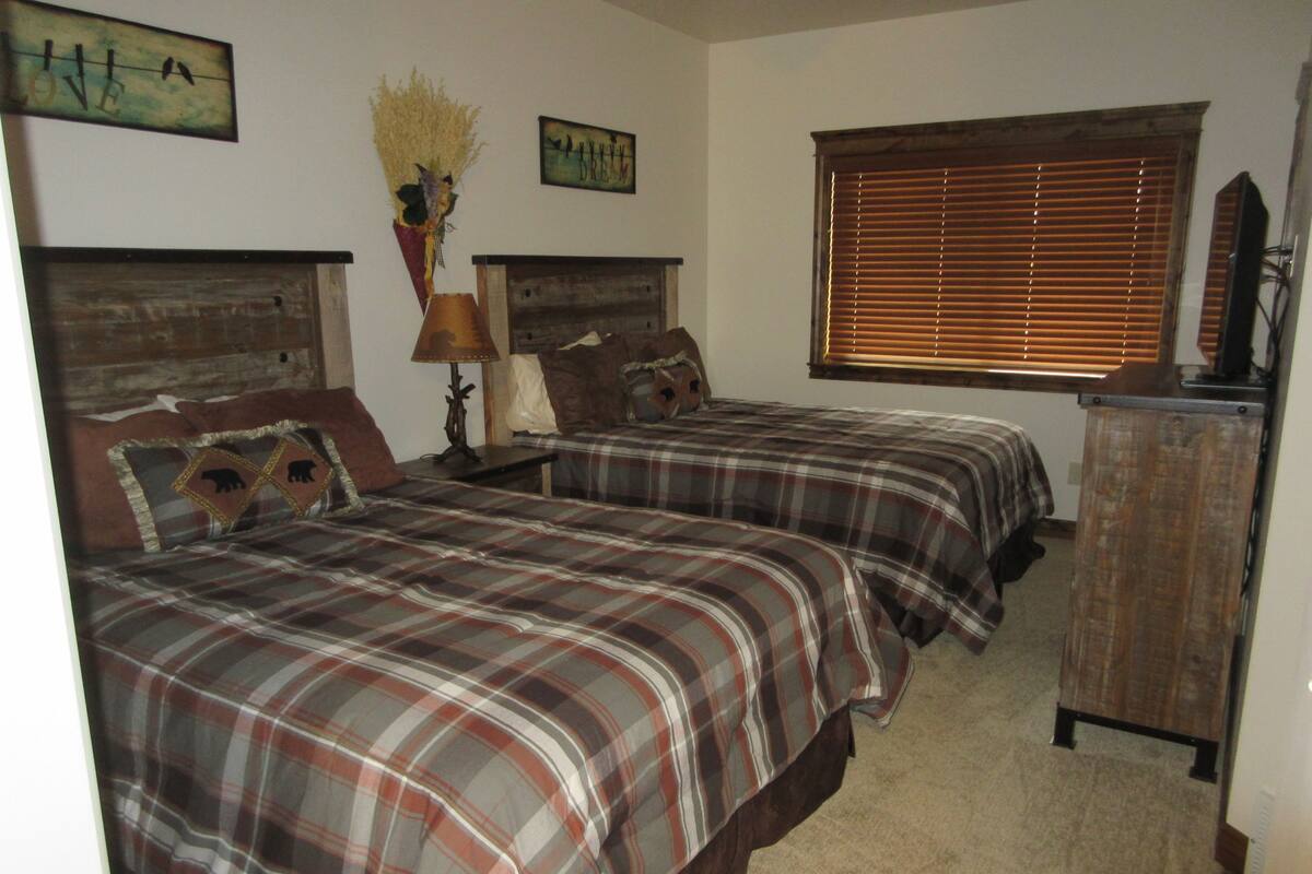 A bedroom with two beds, a dresser, and a window with blinds.