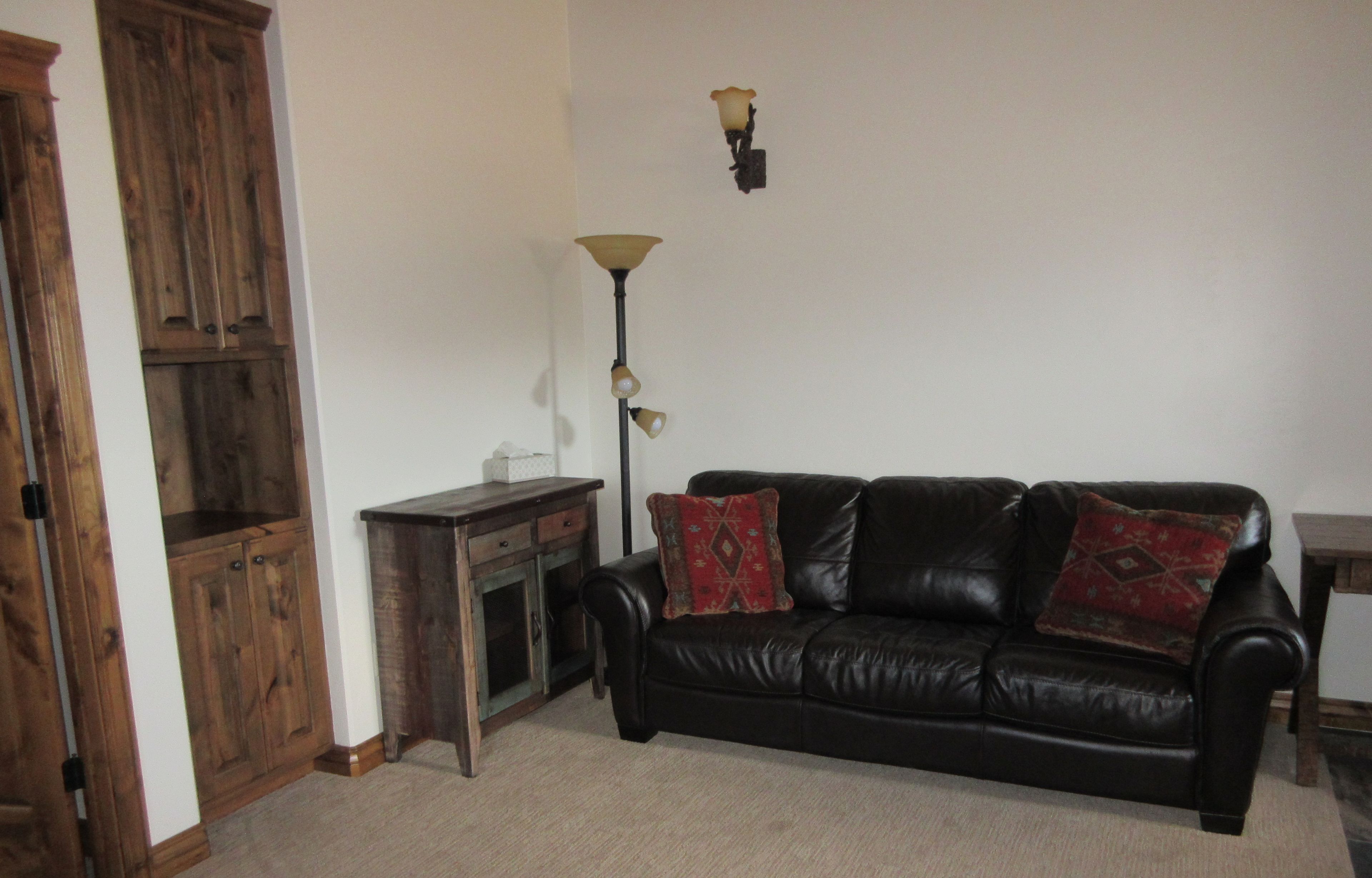 A living room with a black leather sofa, wooden cabinet, and a floor lamp.