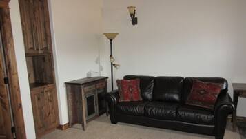 A living room with a black leather sofa, wooden cabinet, and a floor lamp.