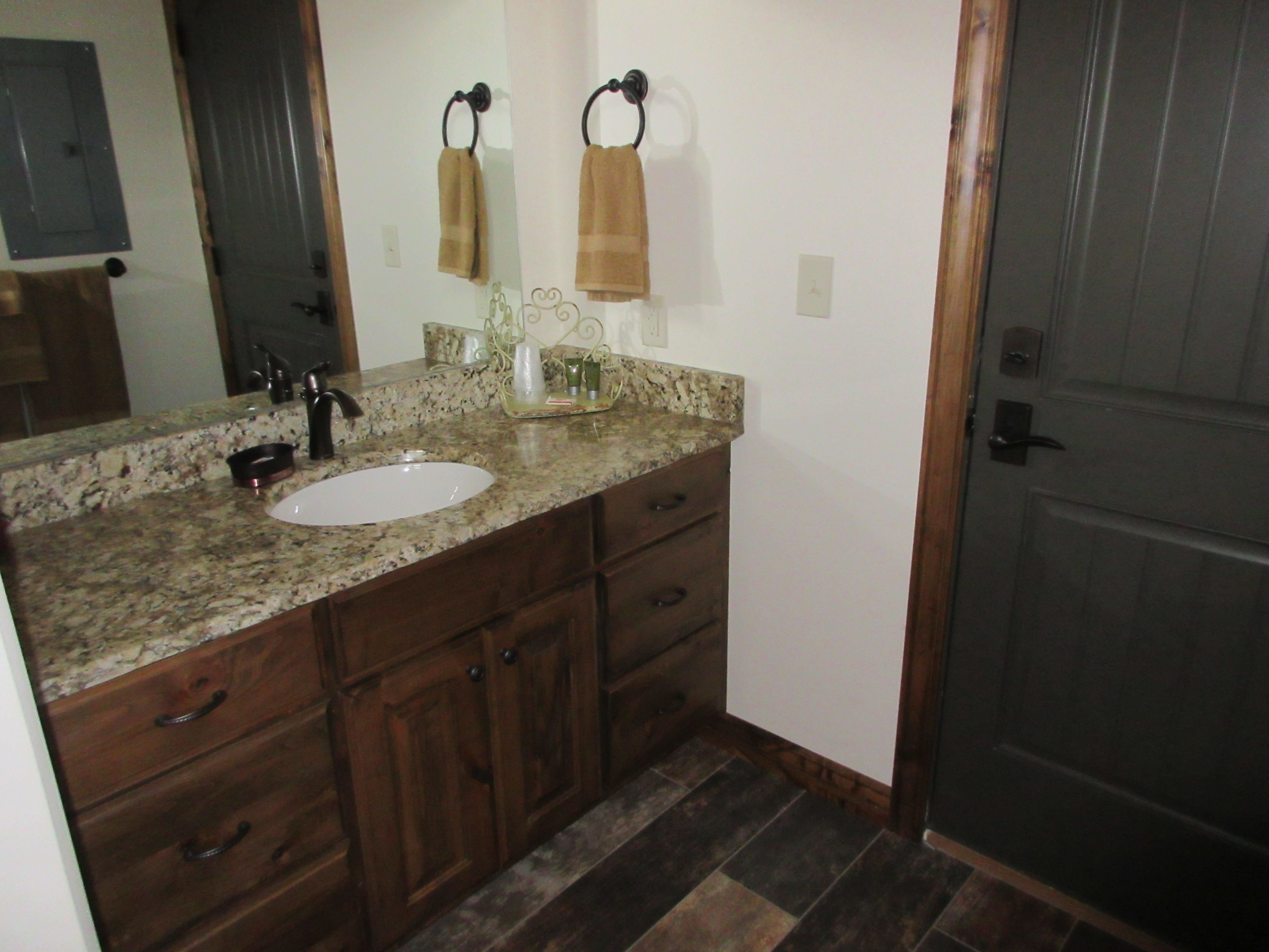 A bathroom with a granite countertop, a white sink, wooden cabinets, and a door with a handle.