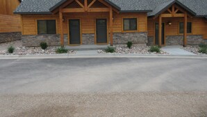 A two-story log cabin with a stone foundation, a front porch, and a driveway. - Townhomes on the Green (Afton)
