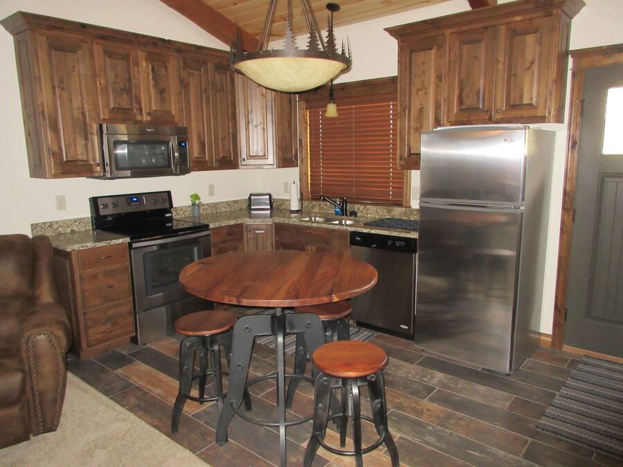 A kitchen with wooden cabinets, a stainless steel refrigerator, a microwave, a stove, and a dishwasher. There is a wooden dining table with stools.