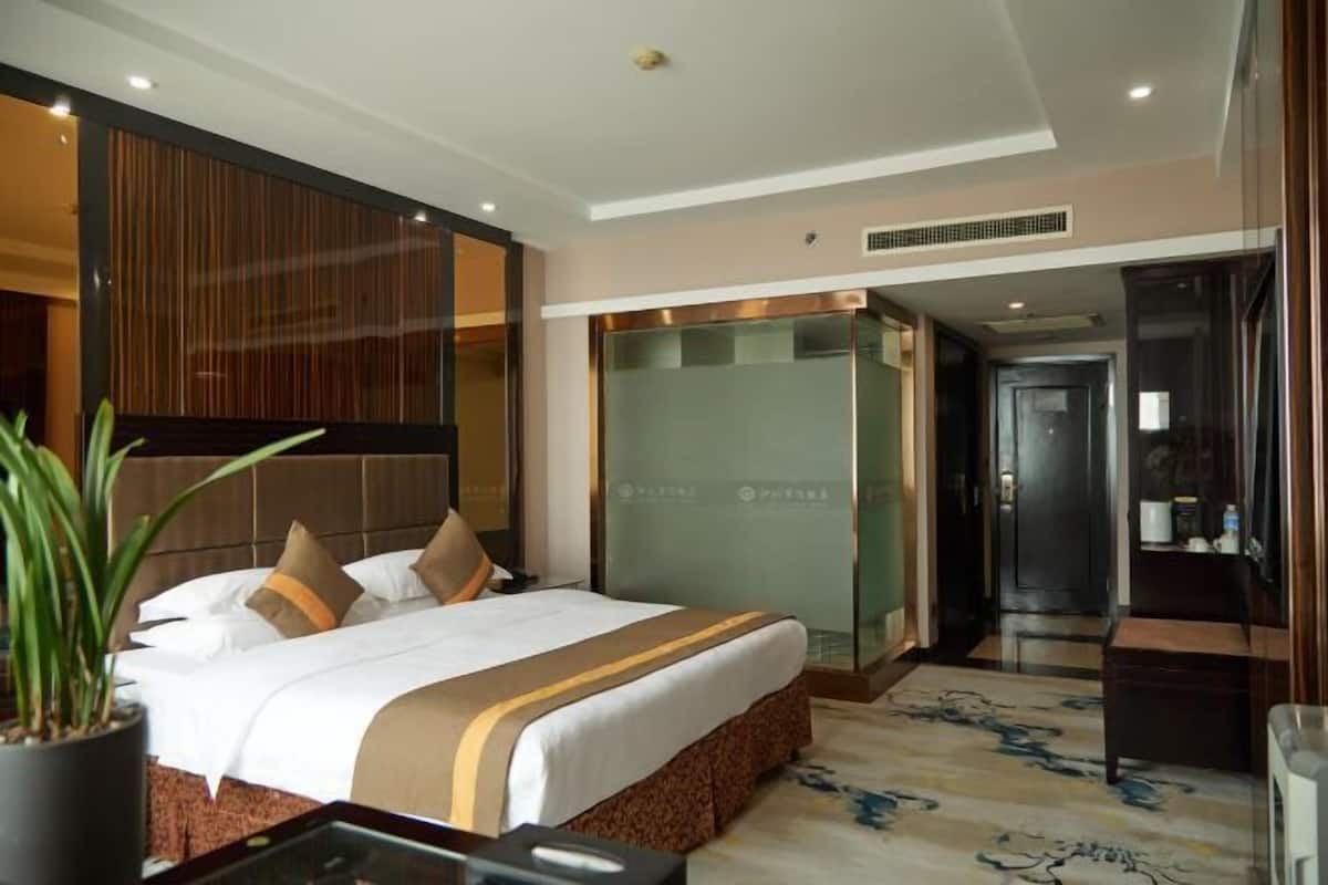A modern hotel room with a large bed, a desk, and a potted plant.