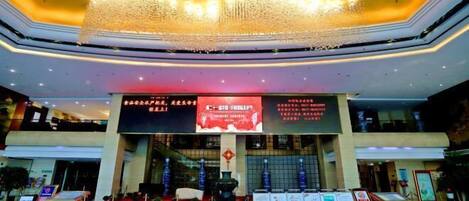 A spacious lobby with a large, ornate chandelier, digital signage, and a reception desk.
