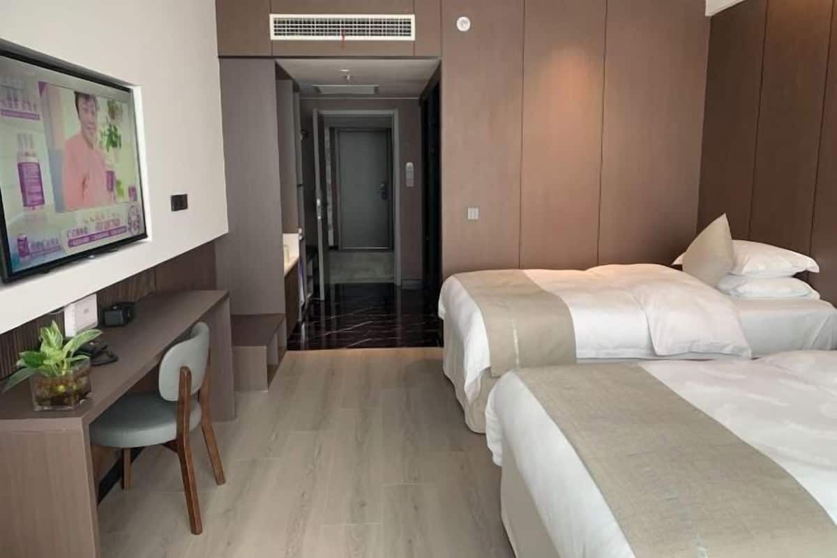 A hotel room with a TV mounted on the wall, a desk with a chair, and two beds with white bedding.