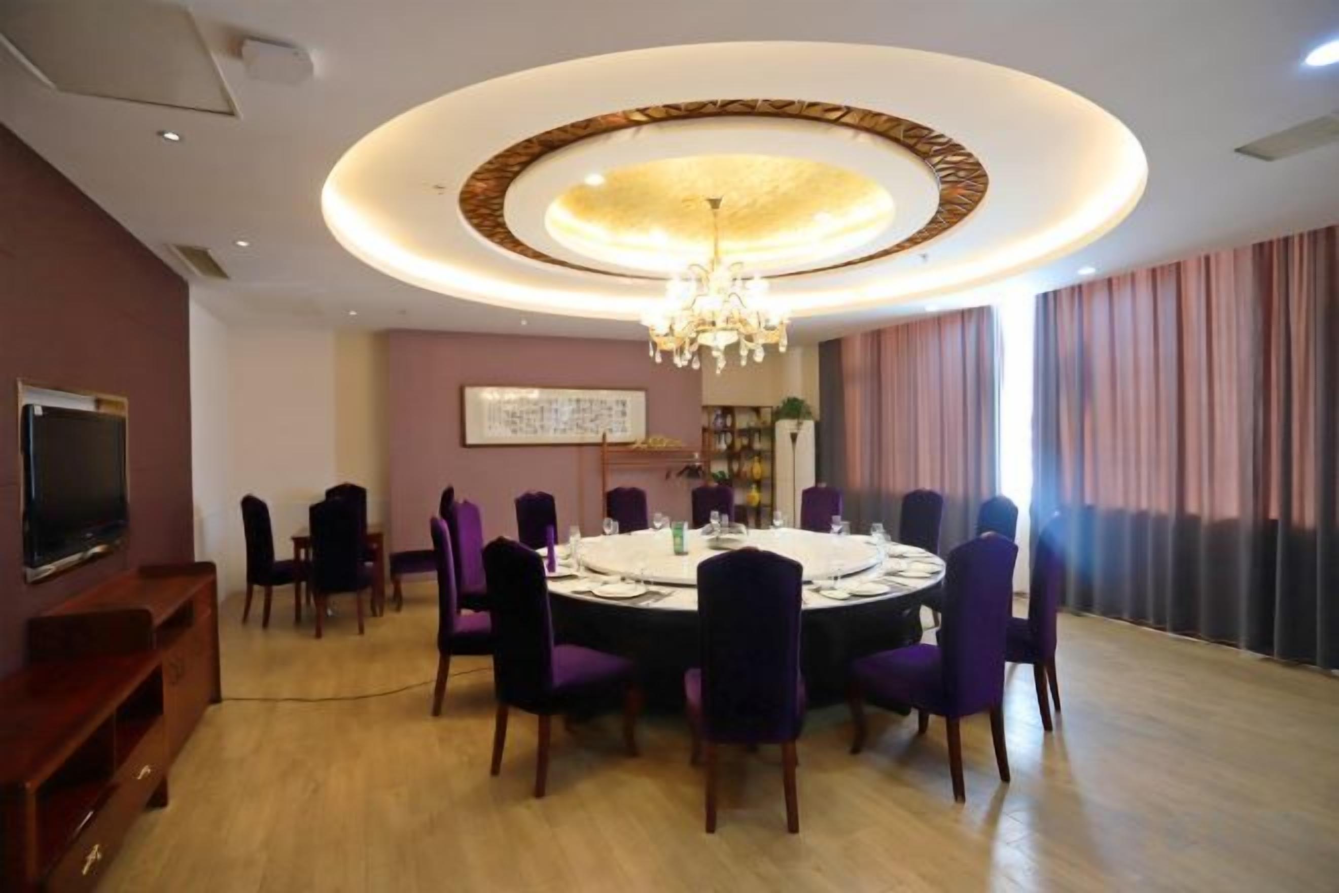 A dining area with a round table, purple chairs, a chandelier, and a television on the wall.