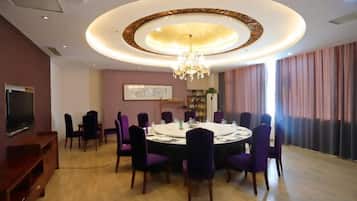 A dining area with a round table, purple chairs, a chandelier, and a television on the wall.