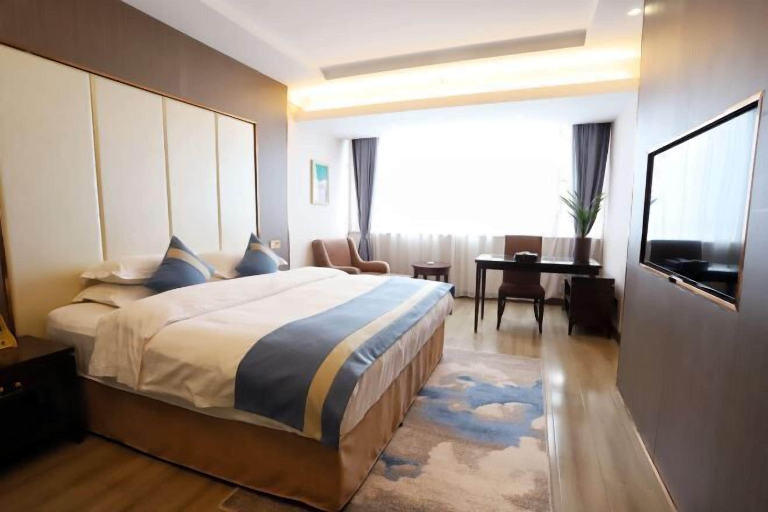A hotel room with a large bed, a desk, and a TV.
