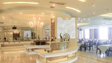 A modern hotel lobby with a central reception desk, seating areas, and a chandelier.