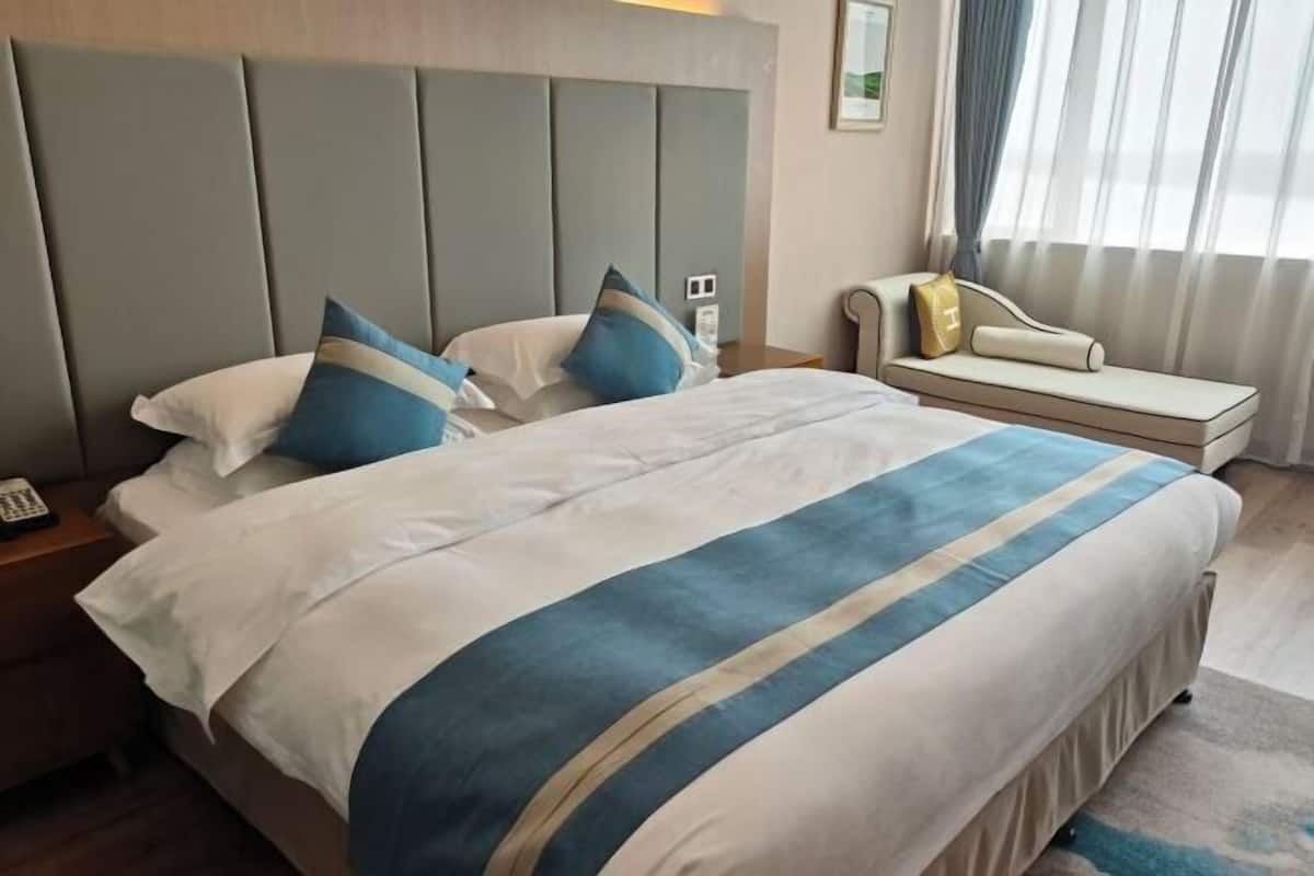 A hotel room with a large bed, a headboard, a bedside table with a phone, and a sofa with a cushion.