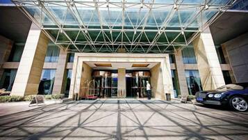L’entrée d’un hôtel, avec un auvent en verre, une voiture garée à l’extérieur et une personne qui se dirige vers l’entrée.