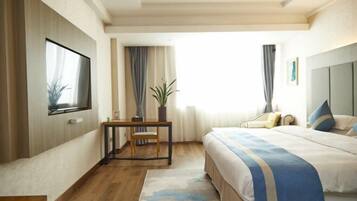A hotel room with a bed, a desk, a chair, a TV, and a window with curtains.