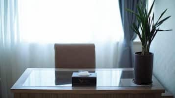 A hotel room with a glass-top table, a tissue box, and a potted plant.