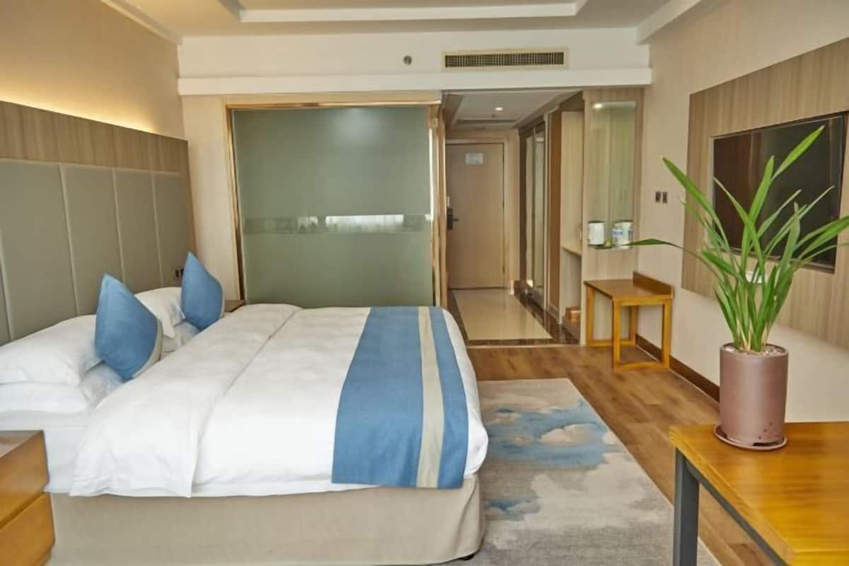 A modern hotel room with a bed, bedside table, and a potted plant.