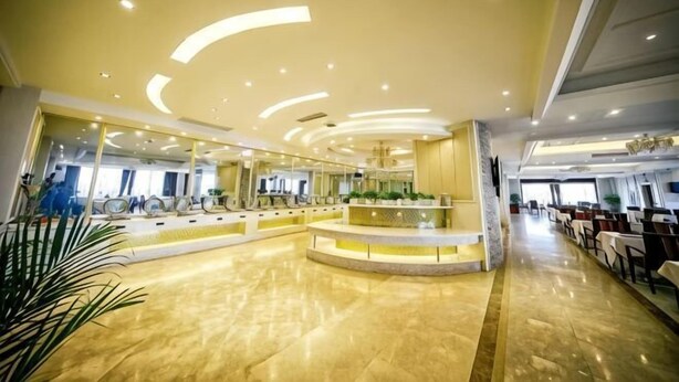 Un'ampia hall con una reception centrale, un soffitto curvo con illuminazione a incasso e un lungo corridoio che conduce a una sala da pranzo.