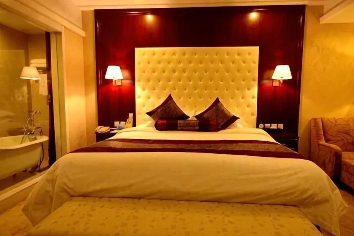 A hotel room with a large bed, a headboard with tufting, two bedside lamps, a nightstand, and a chair.